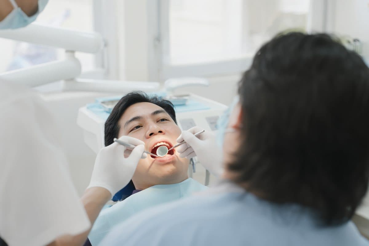 A dentist examining a patient's tooth with a mirror in a bright surgery