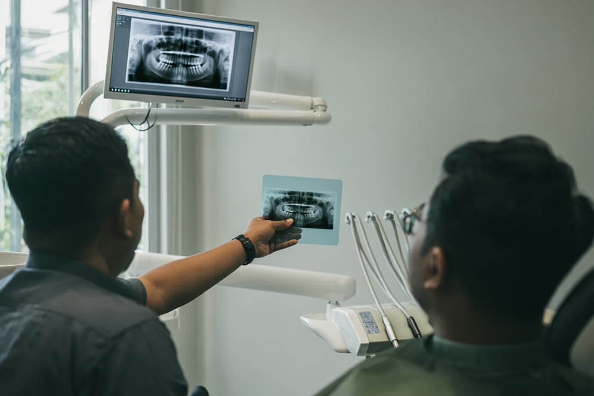A dentist showing a patient a dental x-ray of a wisdom tooth on a monitor